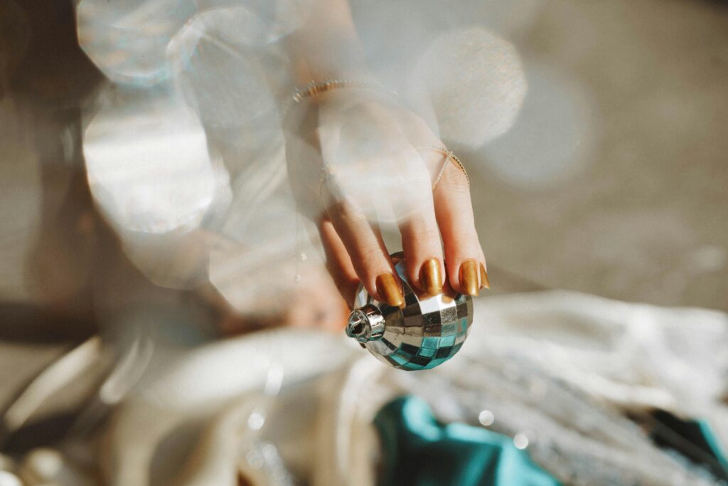 A close-up of a hand with manicured nails holding a shiny Christmas bauble, capturing holiday elegance.